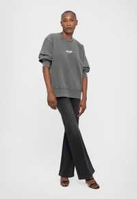 Sudadera gris con cuello redondo y texto impreso, combinada con pantalones de mezclilla oscuros acampanados y sandalias negras de punta abierta. Textura suave, estilo casual.
