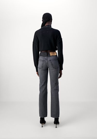Black cropped sweater and gray high-waisted jeans with a straight leg. Textured fabric with visible pocket stitching and branding detail.