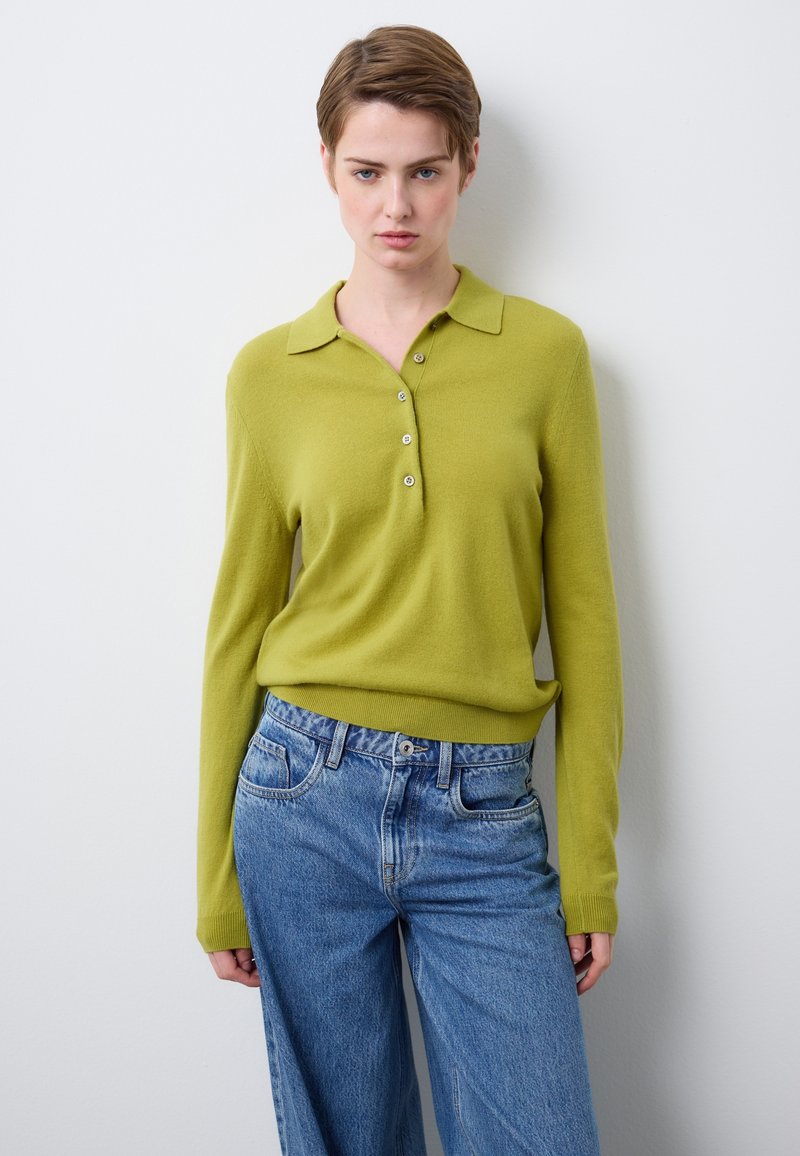 Grüner gestrickter Polopullover mit Kragen und Knopfleiste, kombiniert mit hoch taillierten, hellblauen Jeans mit weitem Bein.