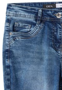 Jean en denim bleu avec poches avant visibles, bouton en métal, passants de ceinture et détails de tissu délavé.