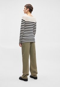 Top de manga longa riscado em preto e creme, combinado com calças largas verde-oliva, exibido de costas com um corte descontraído e decote arredondado.