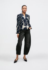 Bluza cu model navy și crem, cu decolteu în V și mâneci lungi, asortată cu blugi largi gri închis și pantofi slingback negri cu vârf ascuțit.