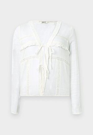 Λευκό πουκάμισο με μακριά μανίκια, λαιμόκοψη σε σχήμα V, διακοσμητικό βολάν, κλείσιμο με κορδόνι μπροστά και κεντητές λεπτομέρειες στο μπούστο και τα μανίκια.