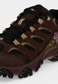 Chaussure de randonnée marron et noire avec des accents jaunes, des lacets noirs, une semelle robuste et le logo Merrell sur le côté.