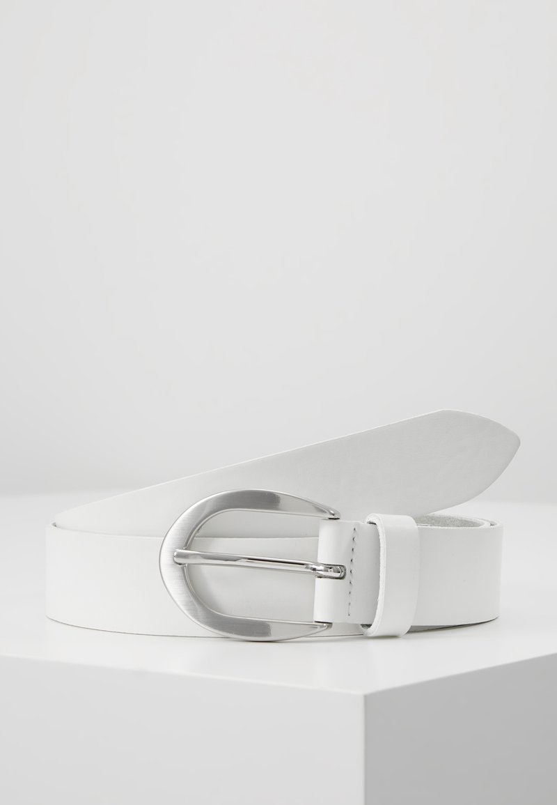 Ceinture en cuir blanc avec une grande boucle ovale argentée polie, enroulée et posée sur une surface blanche sur un fond gris clair.