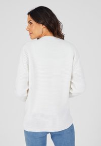 Suéter blanco de punto con un patrón de canalé texturizado, mangas anchas y escote redondeado, combinado con jeans de mezclilla azul claro.