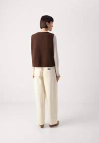 Brown fleece vest with a soft texture, worn over a light ribbed top, paired with cream-colored wide-leg pants and brown heeled shoes.