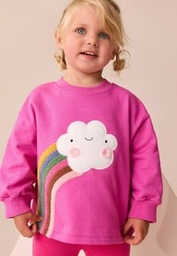 Rosa Baumwoll-Sweatshirt mit einem weißen Wolken-Applikation mit Gesichtszügen und einem bunten Regenbogen-Design aus strukturierten Stoffen.
