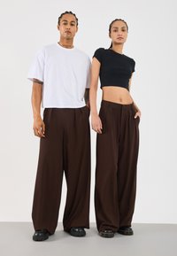 Zwarte cropped top en witte oversized t-shirt gecombineerd met bruine wijde broek. Zwarte chunky schoenen. Gladde stof, minimalistisch ontwerp.