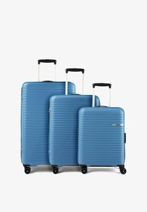 Tre valigie rigide blu con manici neri e quattro ruote, disposte per dimensione dalla più grande alla più piccola su sfondo bianco.