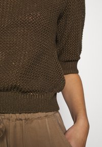 Bruine gebreide trui met korte mouwen en geribbelde zoom, gecombineerd met een lichtbeige, losse, hoog-waist broek met een gestructureerd ontwerp.