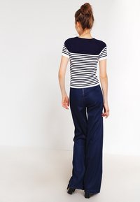Top de manga corta a rayas en azul marino y blanco, con hombros lisos en azul marino, combinado con pantalones de pierna ancha de talle alto en azul oscuro.