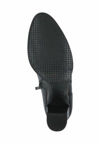 Zapato negro con suela de goma texturizada, que presenta un diseño contorneado y una pequeña correa. Material superior suave con detalles de costura.