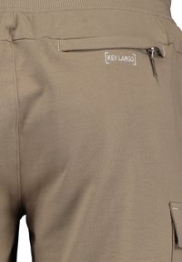 Pantaloni della tuta beige con tasca laterale con zip, vita elasticizzata e logo ricamato. Tessuto morbido e design casual.