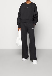 Czarny zestaw bluz i spodni dresowych z krótkim krojem, z białym logo Nike na klatce piersiowej i nogawce, w połączeniu z białą torbą.