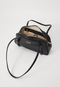 Bolso de mano de piel negra con textura suave, cierre de cremallera y una sola correa ajustable. El interior presenta un forro claro y bolsillos.