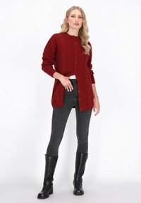 Czerwony dzianinowy kardigan z plecionymi wzorami, zapinany na guziki, z prążkowanymi mankietami, zestawiony z czarnymi skinny jeansami i czarnymi botkami do kolan.