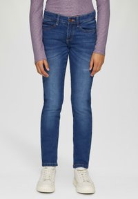 Ciemnoniebieskie slim fit dżinsy z zapięciem na guzik z przodu, pięcioma kieszeniami i zblakłymi akcentami; w połączeniu z kremowymi trampkami.