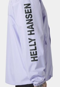 Light lavender waterproof jacket with black "HELly Hansen" text along the sleeve, featuring elastic cuffs and a sleek, smooth texture.