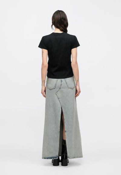 Zwart T-shirt met korte mouwen, gecombineerd met een lange, lichtgrijze denim rok met een voorste split en contrasterende naden. Zwarte enkellaarzen zichtbaar.