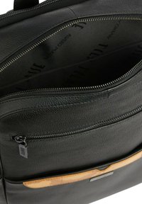 Borsa in pelle nera con finitura testurizzata, dotata di un compartimento principale con zip e un accento beige a contrasto nella parte inferiore.