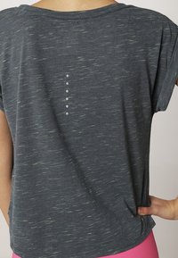 Mörkgrå t-shirt med korta ärmar och en strukturerad mönstring. Har en subtil design av sex vertikala prickar längs ryggen.