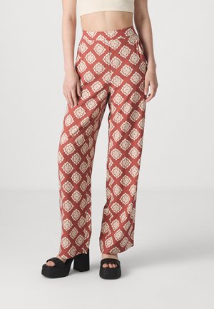 Pantalons larges à motifs rouges avec un design floral en crème. Caractéristiques d'une taille haute et d'une texture de tissu lisse. Portés avec des sandales à plateforme noires.
