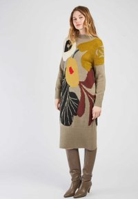 Robe tricotée beige avec un motif floral en jaune, rouge et noir ; ourlet côtelé ; manches longues ; associée à des bottes marron jusqu'au genou.