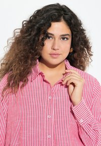 Camicia a righe rossa e bianca con bottoni, realizzata in tessuto leggero, dotata di colletto e maniche con risvolto decorate da bottoni.