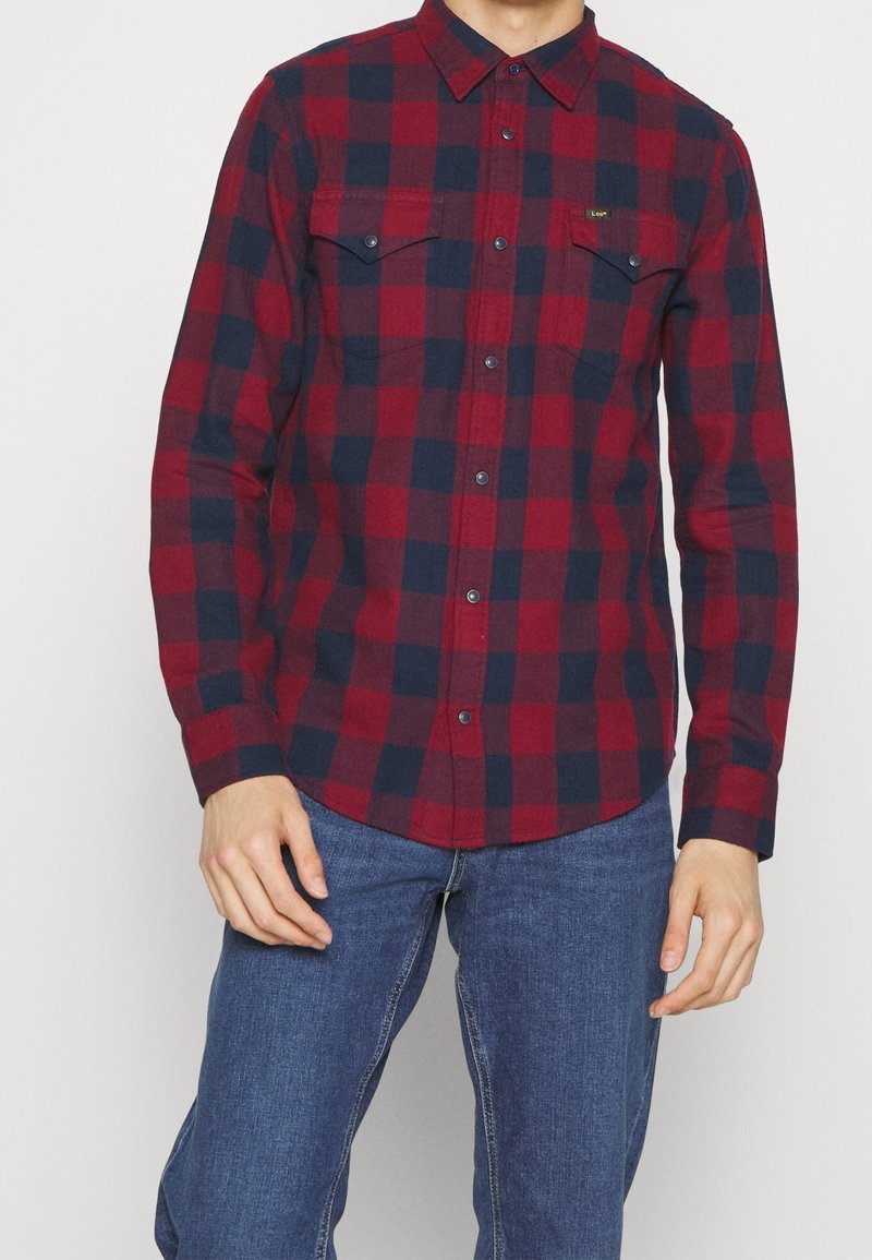 Rød og marineblå plaid flannel skjorte med knap-ned krave, to brystlommer og frontknapper. Stoffet har et blødt, tekstureret udseende.