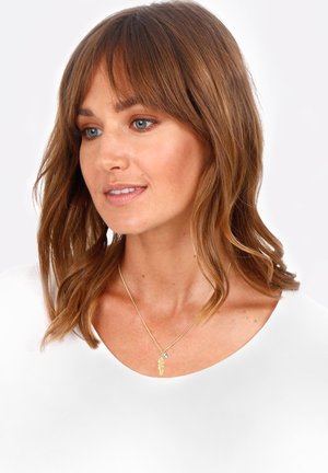 Goldene Halskette mit einem Federanhänger und einem kleinen Kristallakzent, getragen über einem schlichten weißen Oberteil. Klare Linien und minimalistisches Design.