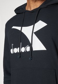 Felpa blu navy con un grande logo e scritte bianche. Ha una tasca a marsupio e un cordino sul cappuccio. Materiale in cotone morbido con una vestibilità comoda.