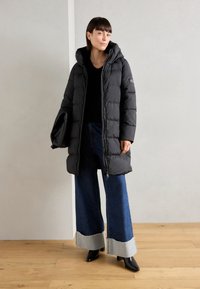 Black puffer coat with a hood, featuring a zip front and quilted texture. Worn over dark wide-leg jeans with a gray hem. Black footwear.