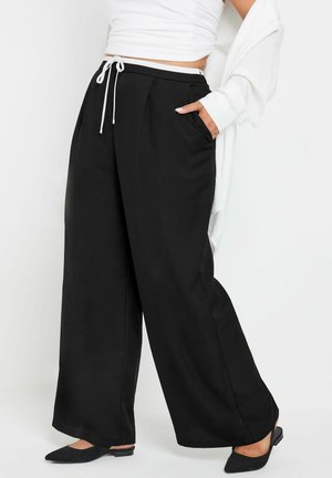Zwarte wijde broek met een elastische tailleband, voorzien van zijzakken en een zachte textuur, gecombineerd met een losse witte top.