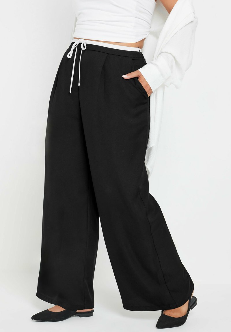 Svarta vida byxor med dragsko i midjan, med sidofickor och en mjuk textur, stylade med en lös vit topp.