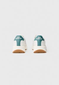 Weiße Sportschuhe mit türkisfarbenen Akzenten, ausgestattet mit einem gepolsterten Kragen, einer strukturierten Gummisohle und dem "New Balance"-Logo an der Ferse.