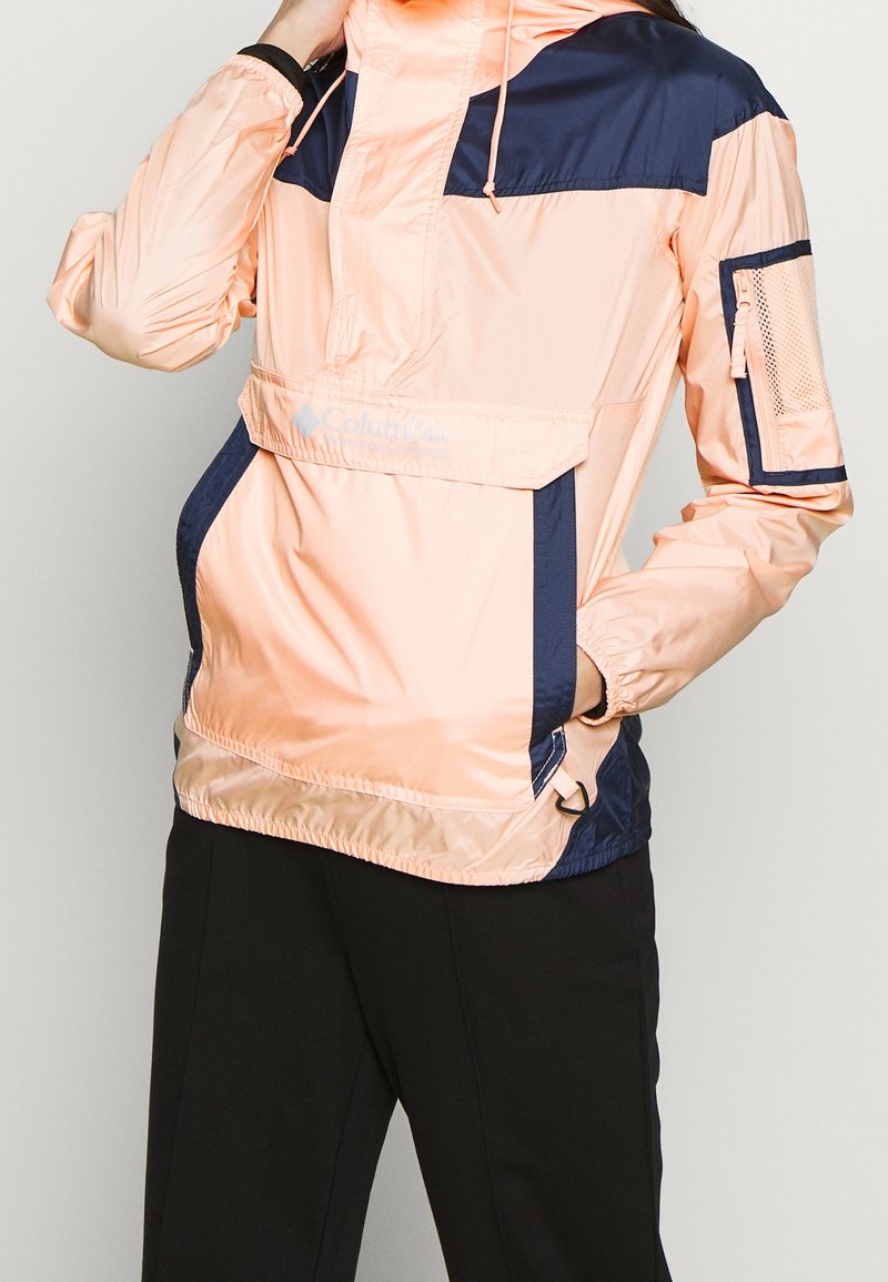 Lättviktsanorak i persika och marinblått. Har en halvdragkedja, elastiska ärmslut, framficka och sidoficka med meshdetalj.