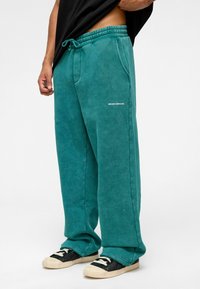 Teal joggings gemaakt van zachte stof met een elastische tailleband, zijzakken en een klein wit "MISSION COMPLETED" tekstdetail.