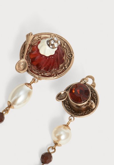 Boucles d'oreilles style vintage avec une mini tasse et assiette à thé, un dessert en pierre rouge, une cuillère en or et des perles sur fond blanc.