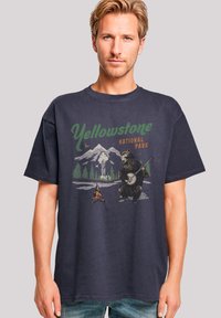 Navyblaue Baumwoll-T-Shirt mit einem Grafikdesign eines Bären, der Banjo spielt, mit dem Text "Yellowstone Nationalpark" und Berglandschaft im Hintergrund.