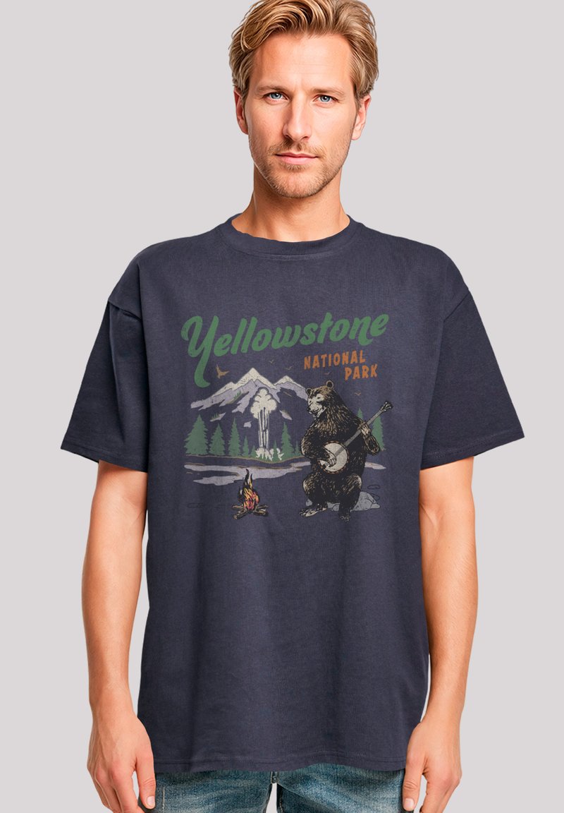 Navyblaue Baumwoll-T-Shirt mit einem Grafikdesign eines Bären, der Banjo spielt, mit dem Text "Yellowstone Nationalpark" und Berglandschaft im Hintergrund.