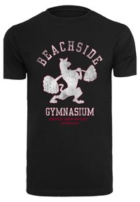 Melna kokvilnas T-kreklā ar attēlu par cēlāju govij, ar baltām un sarkanjām ciparām tekstā "BEACHSIDE GYMNASIUM" un citiem pasvītrojumiem.