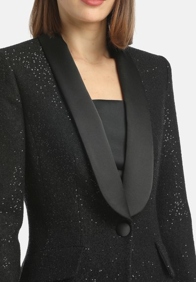 Czarna marynarka z cekinami, z satynowymi klapami, zapinana na jeden guzik, z dwiema bocznymi kieszeniami, prezentująca teksturowany materiał i elegancki design.