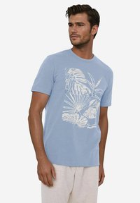 Hellblaues T-Shirt mit kurzen Ärmeln, das auf der Vorderseite ein weißes Design eines tropischen Blattes zeigt. Hergestellt aus weichem Baumwollstoff.