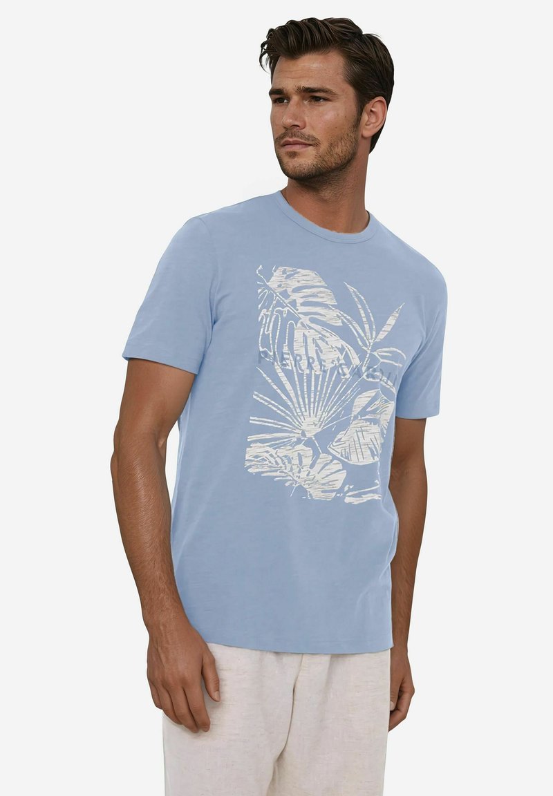 Hellblaues T-Shirt mit kurzen Ärmeln, das auf der Vorderseite ein weißes Design eines tropischen Blattes zeigt. Hergestellt aus weichem Baumwollstoff.