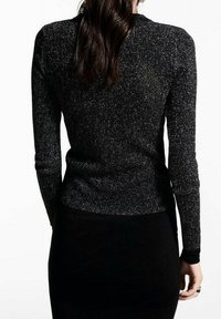 Schwarzes Langarmshirt mit schimmernder Textur, tailliertem Schnitt und gerippten Schultern, kombiniert mit einem figurbetonten schwarzen Rock.