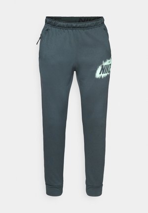 Pantaloni de jogging gri închis, confecționați dintr-un material moale, având talie elastică, buzunare laterale și un mare logo Nike alb cu efect de spray.