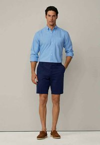 Light blue button-up shirt with long sleeves, paired with dark navy shorts and brown loafers. Simple, fitted design.