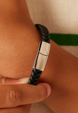 Zwarte gevlochten leren armband met een zilverkleurige metalen sluiting, met een gladde textuur en een veilig sluitontwerp.