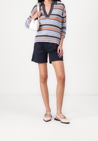 Randig stickad tröja med V-ringning, korta ärmar, marinblå shorts och ljusrosa skor med spänne. Liten vit handväska ingår.